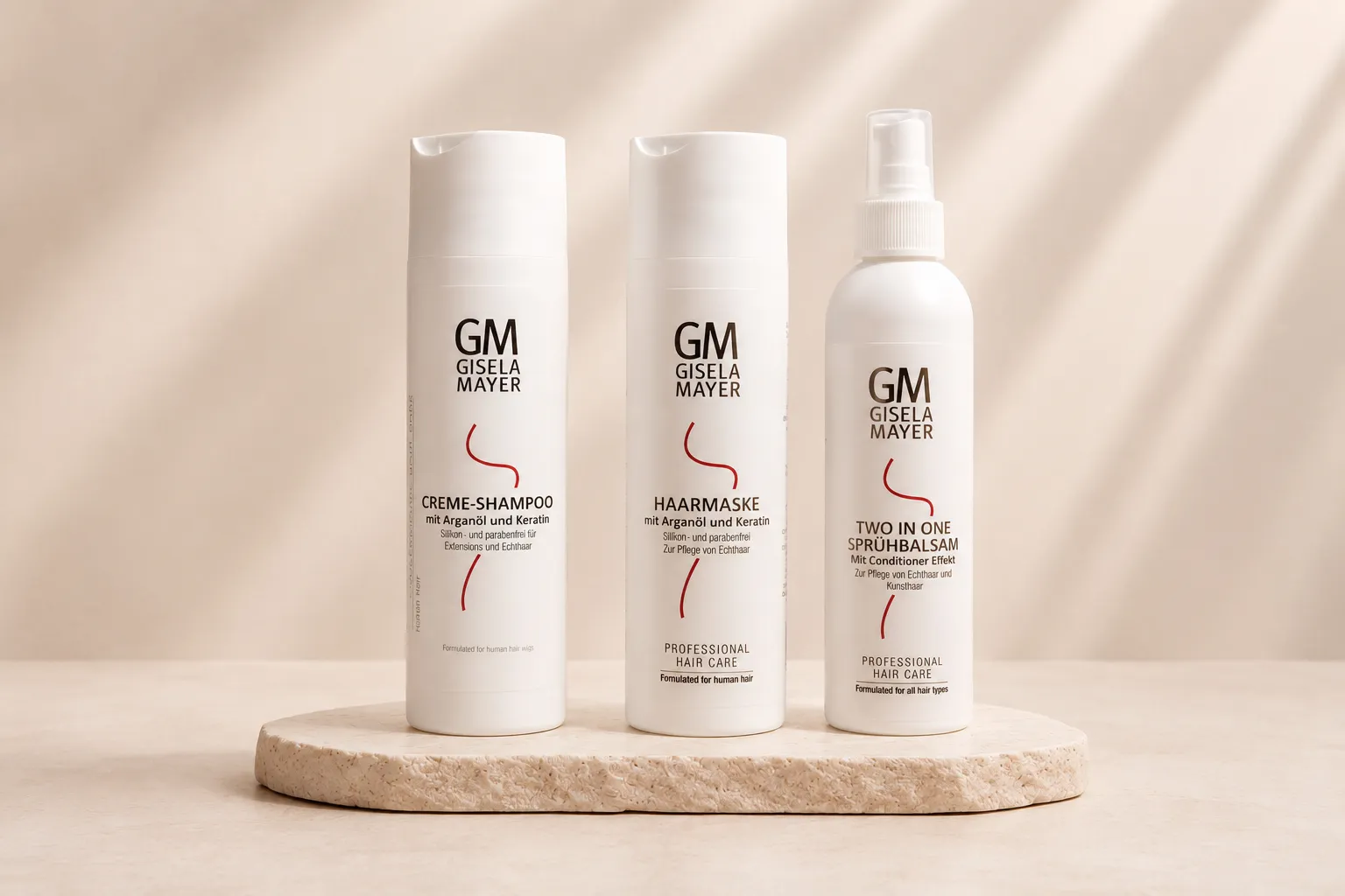 Gisela Mayer crèmeshampoo, haarmasker en two-in-one sprayconditioner met arganolie en keratine, naast elkaar op een natuurstenen plateau.